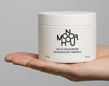 Hand holding a white container with 'Moorhou' branding against a gray background